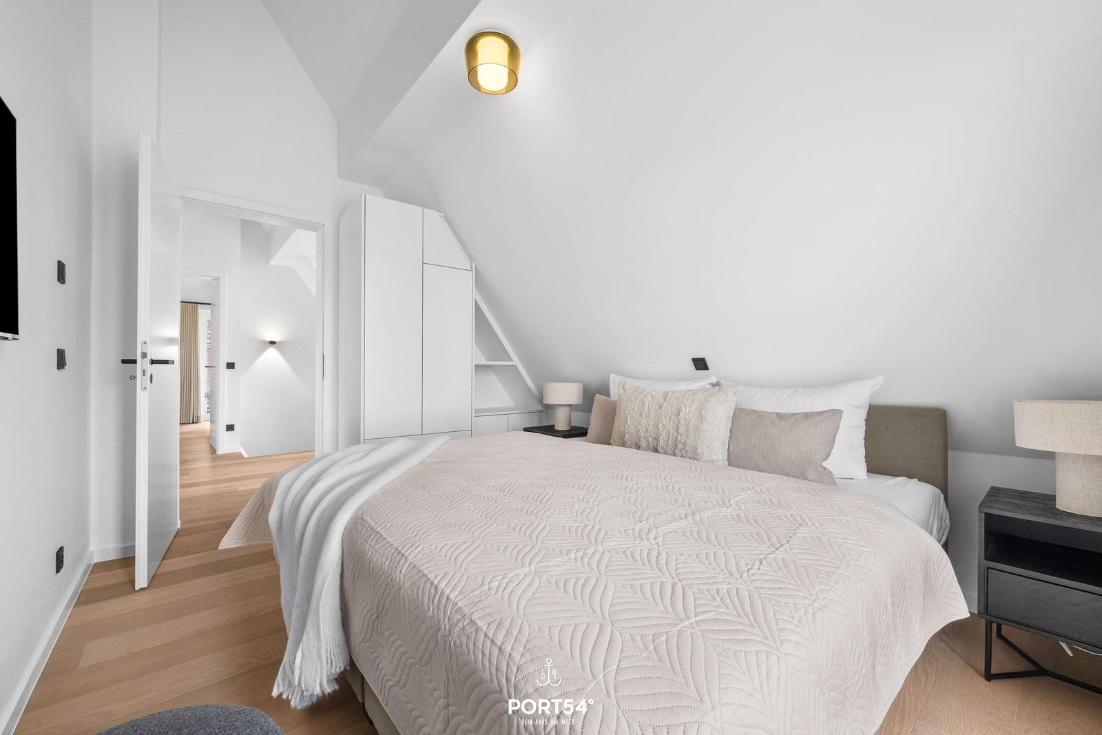 Schlafzimmer mit Bett, Nachttischen und Schrank unter Dachschrägen.