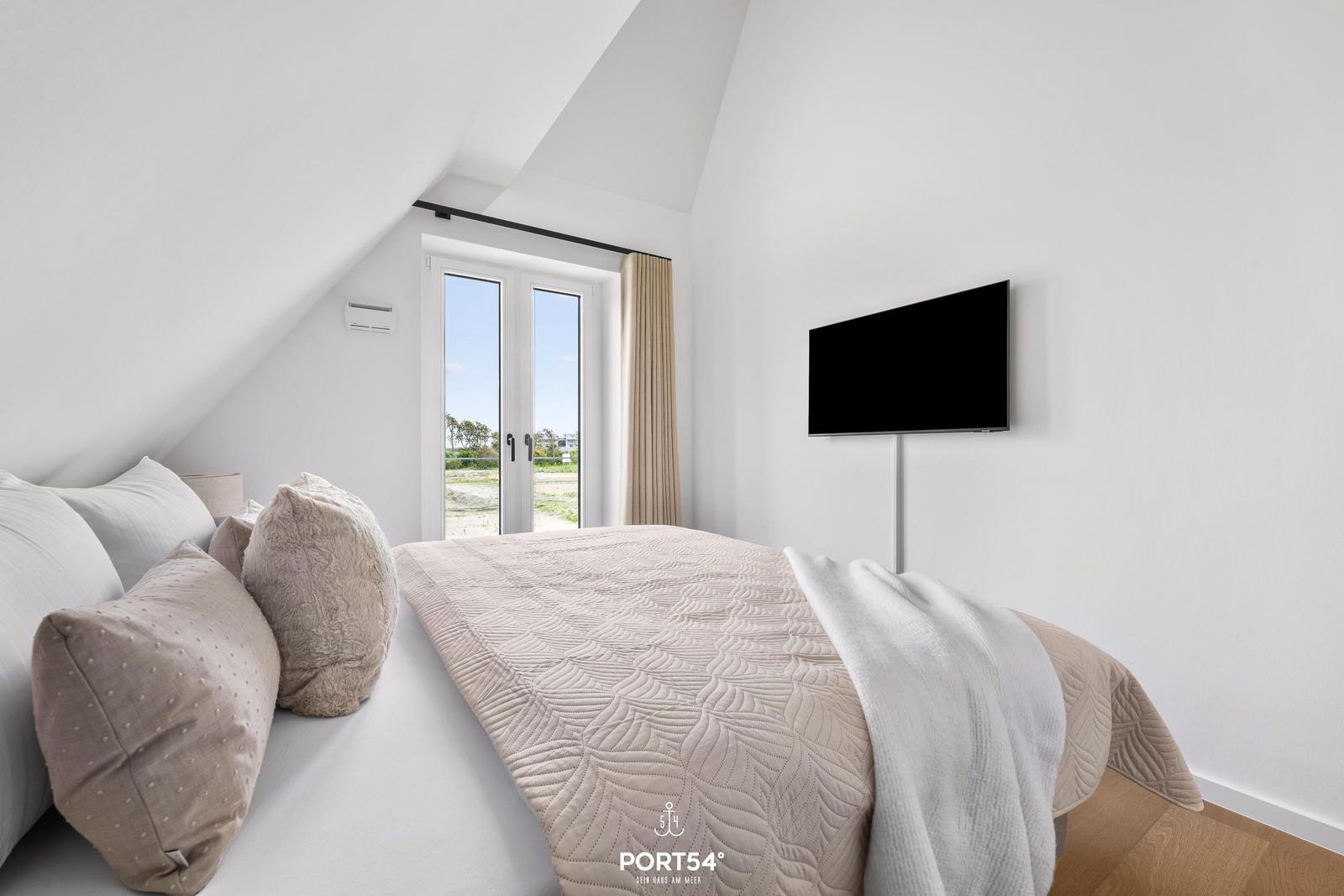 Schlafzimmer mit Dachbodenfenster, Bett und Wandfernseher.