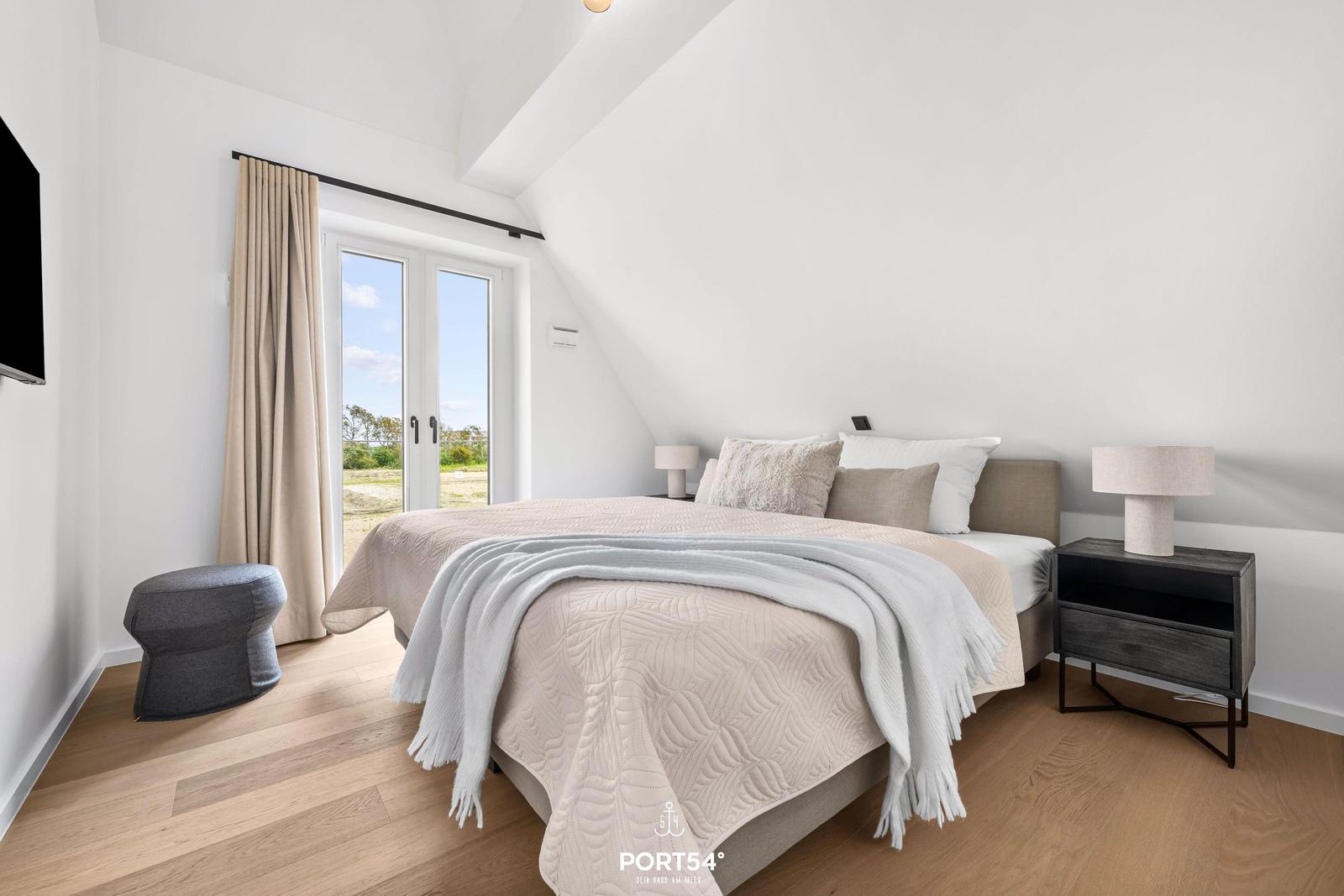 Schlafzimmer mit Doppelbett, Fenster und Holzboden.