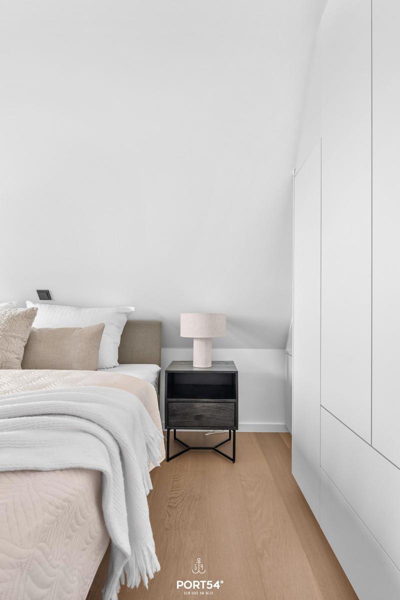 Schlafzimmer mit Bett, Nachttisch und Kleiderschrank. Holzdielenboden und weiße Wände.