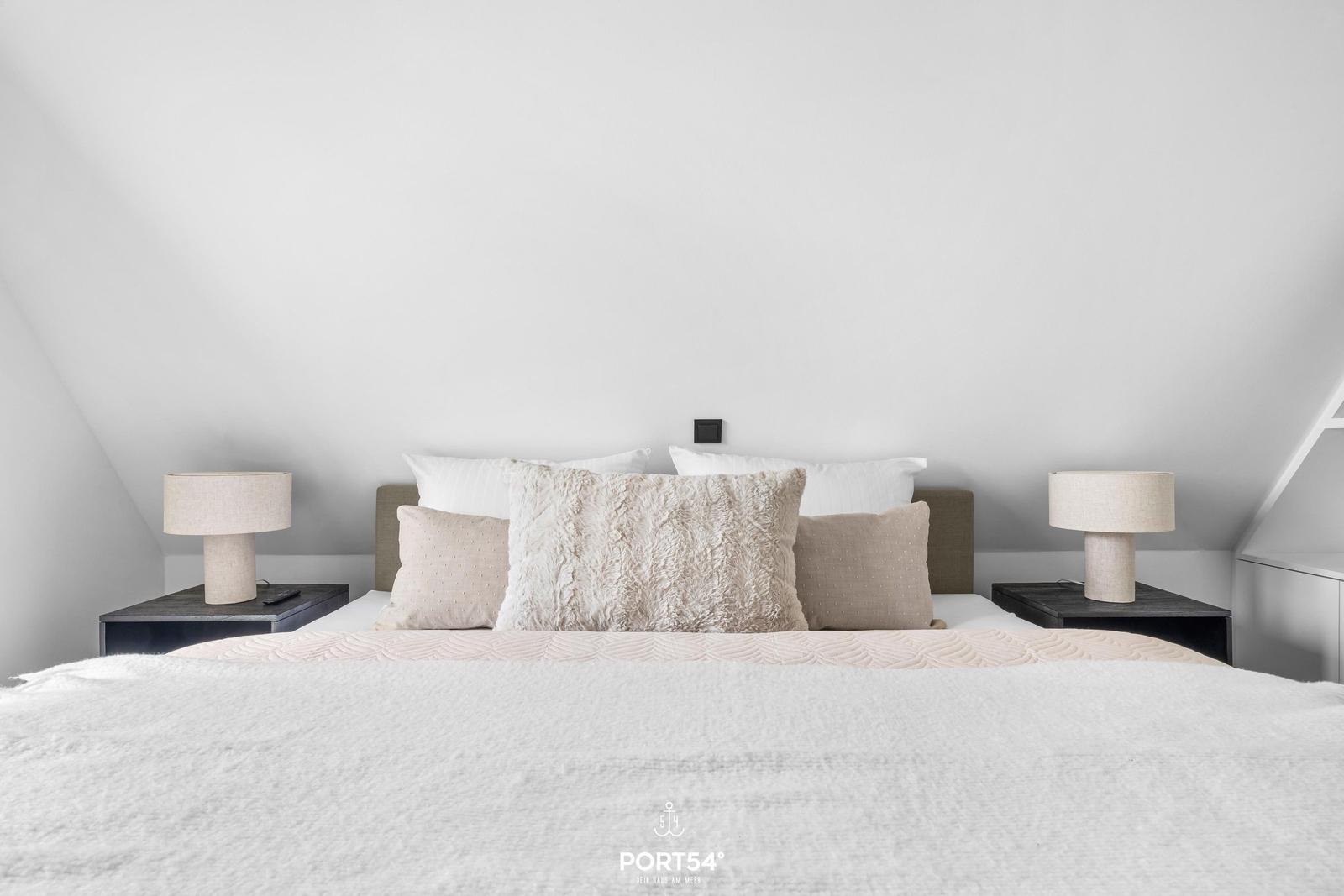 Schlafzimmer mit Dachschräge, Bett mit Kissen und zwei Nachttischen mit Lampen.