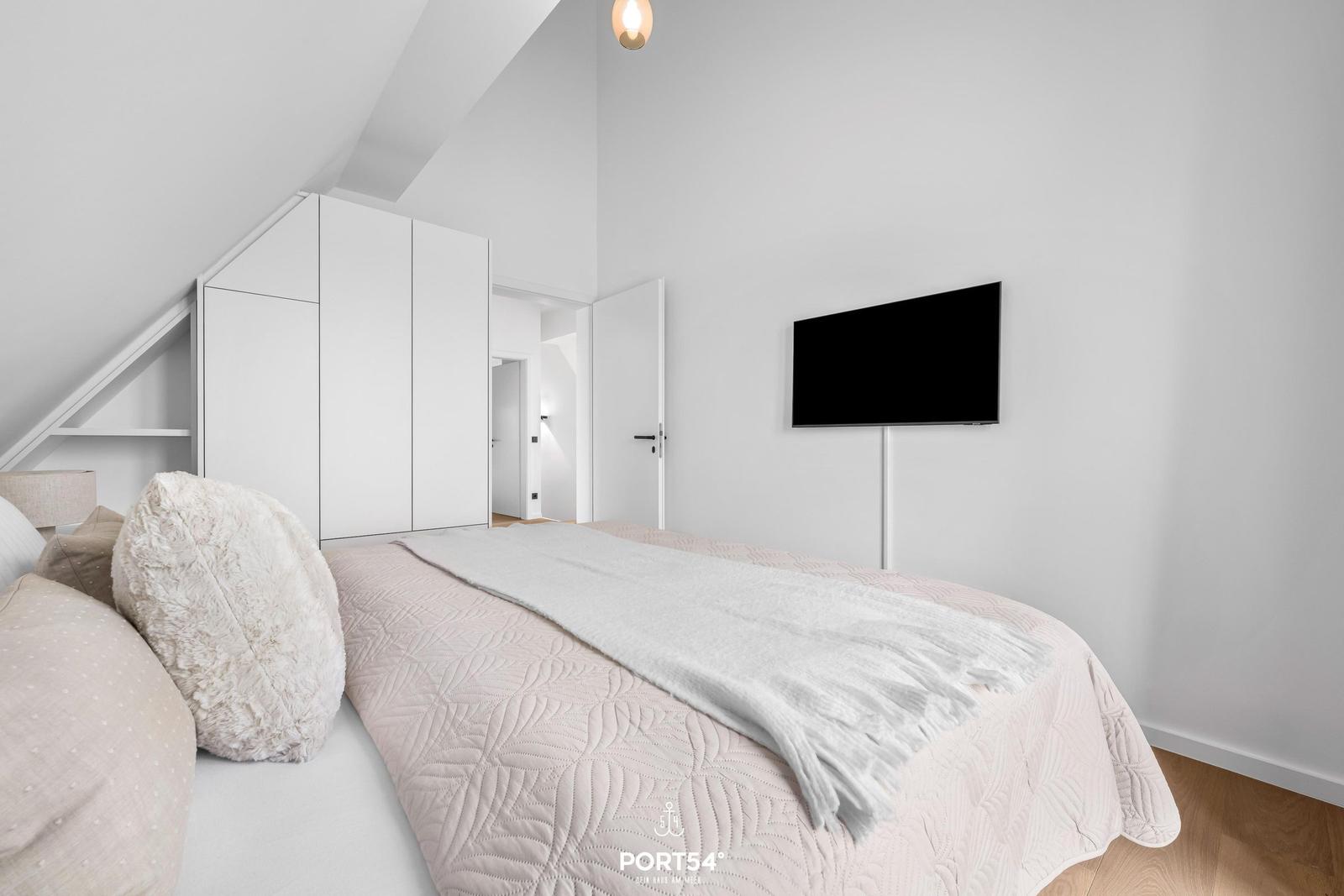 Schlafzimmer mit Bett, Kleiderschrank und Wand-TV. Dachschrägen und Holzboden.