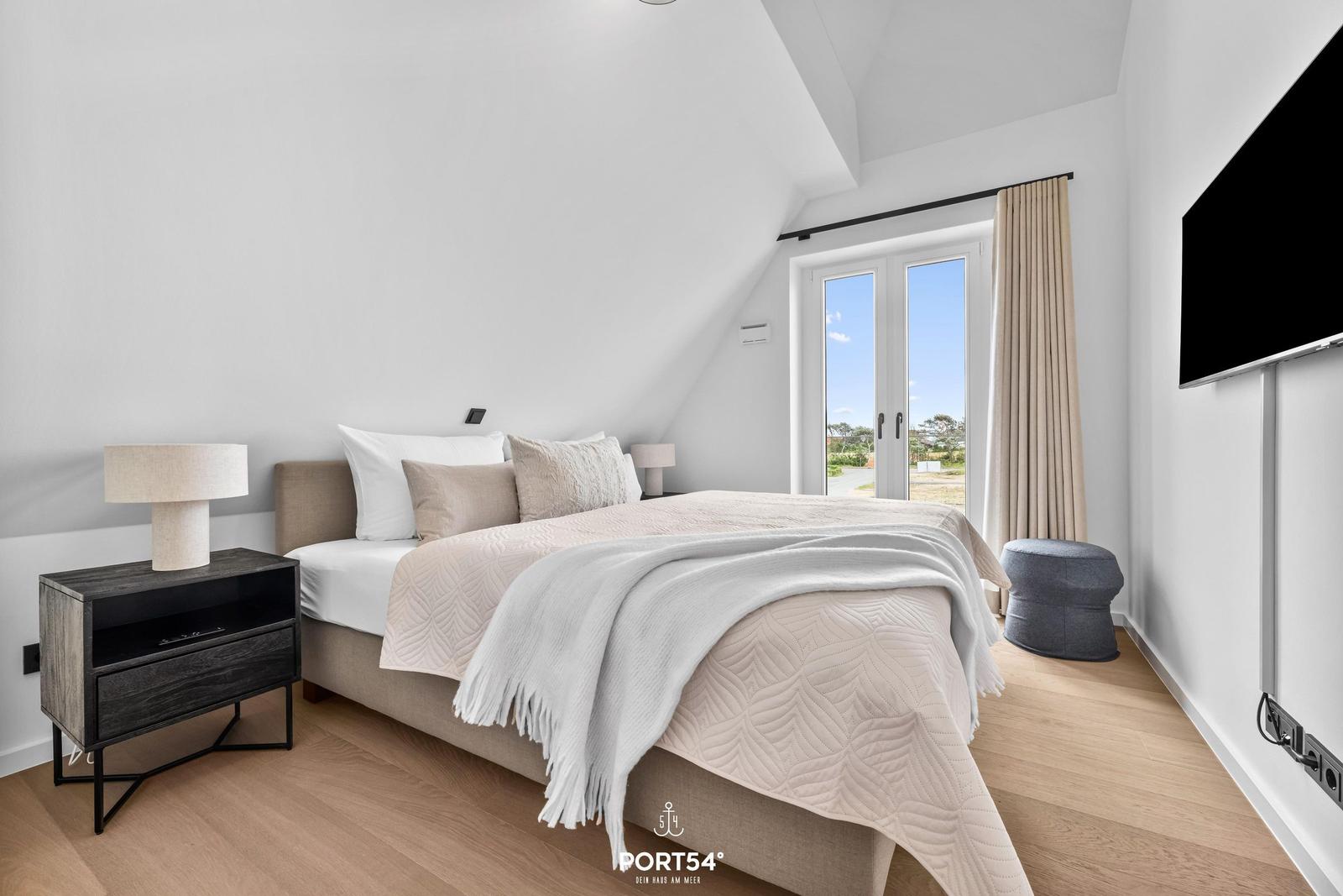 Schlafzimmer mit Dachschrägen, Bett, Nachttisch, Fenster und Fernseher.