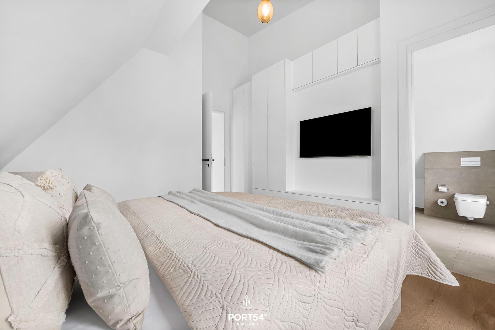 Schlafzimmer mit Bett, TV und angrenzendem Bad.