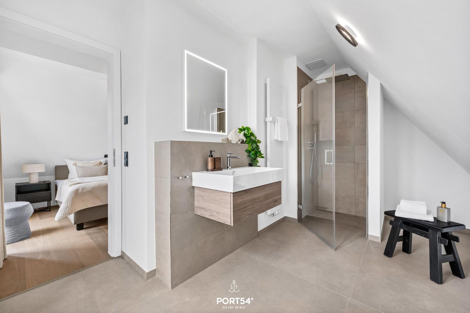 Badezimmer mit Dusche, Waschbecken und Blick in Schlafzimmer