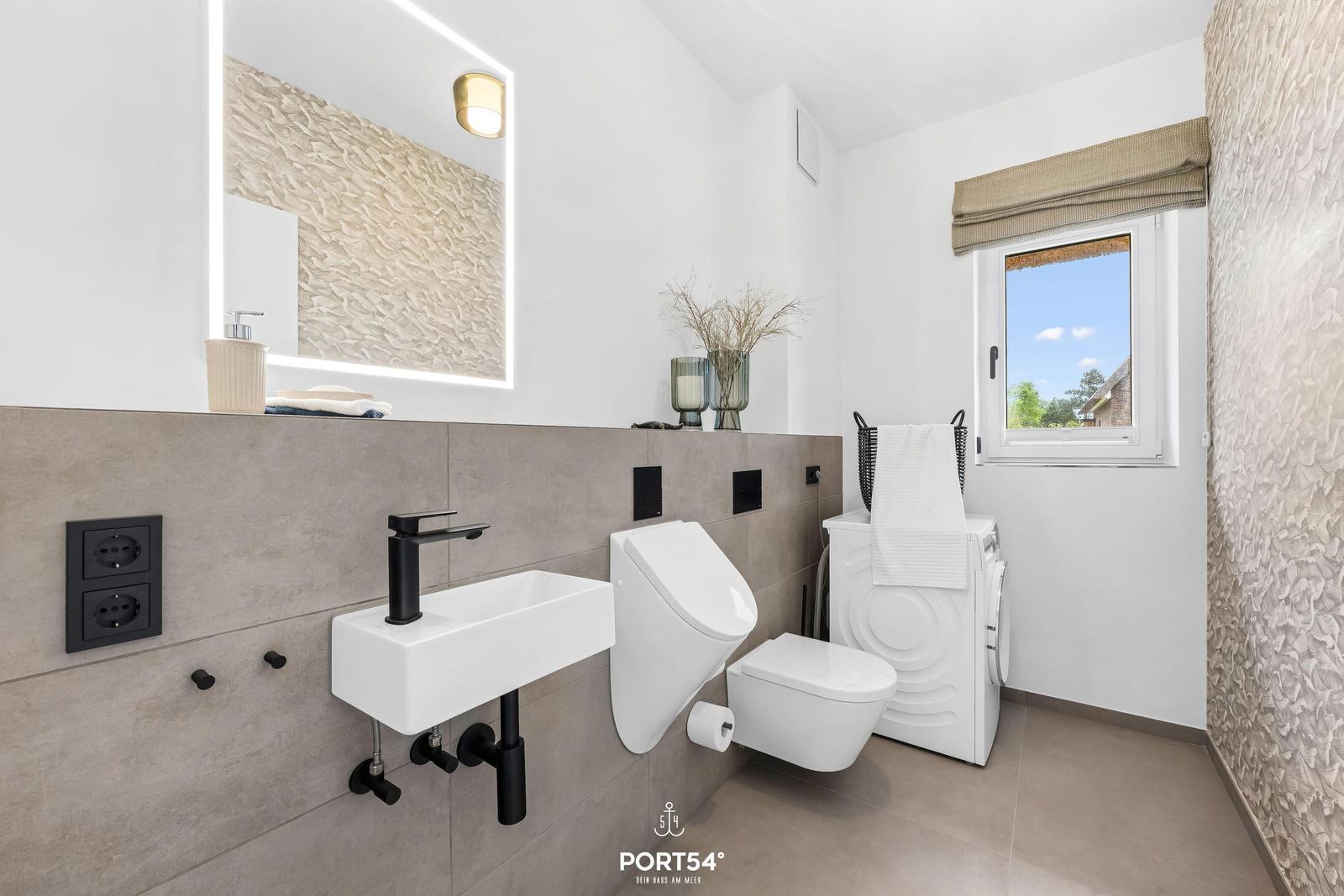Badezimmer mit Waschbecken, WC und Waschmaschine. Fenster mit Blick nach draußen.