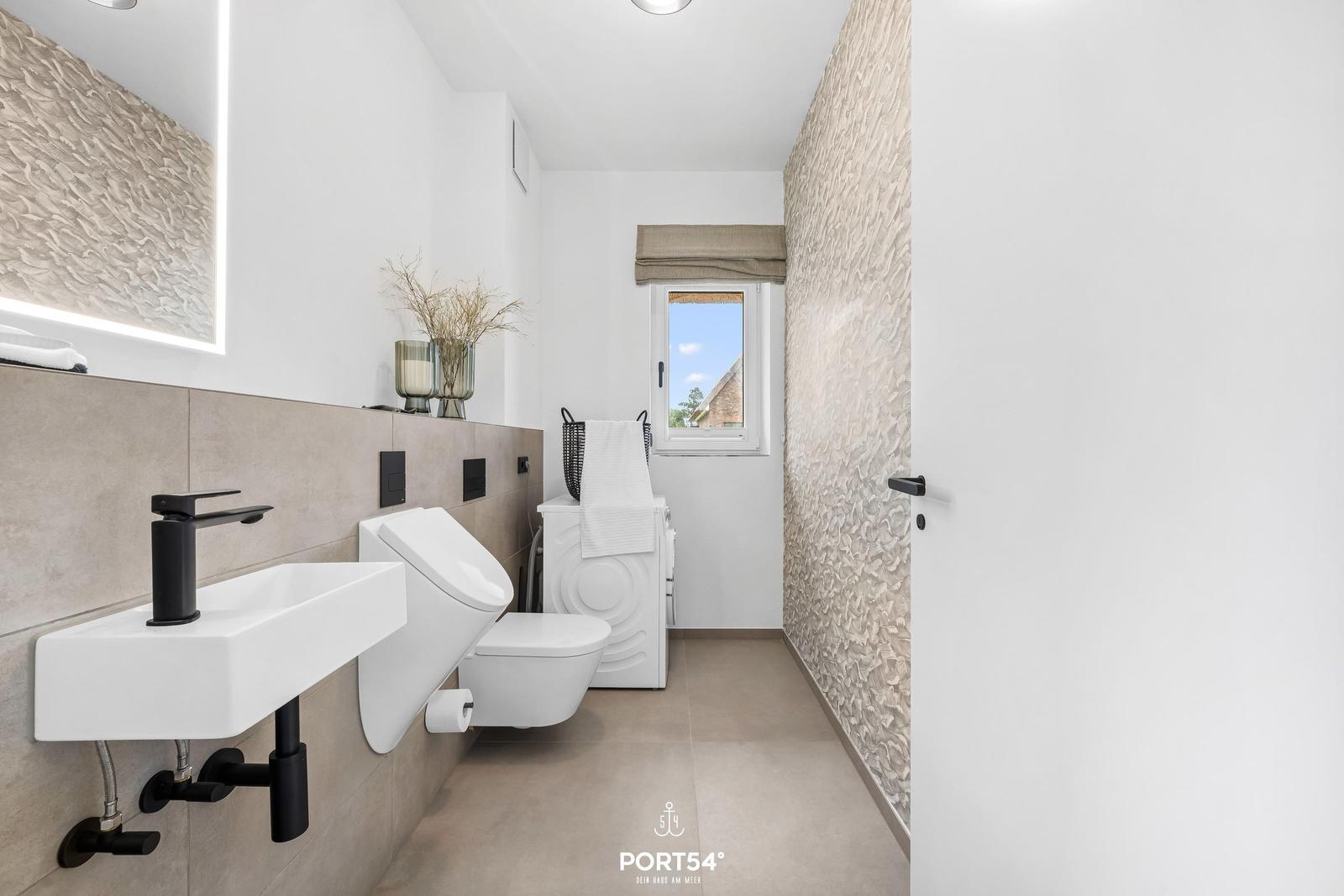 Moderne Badezimmer mit Waschbecken, WC und Fenster. Wandverkleidung und Spiegel mit Beleuchtung.