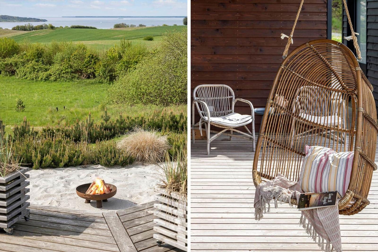 Terrasse mit Feuerkorb und Aussicht auf Grünland und Wasser. Hängesessel und Stühle auf Holzdecke.