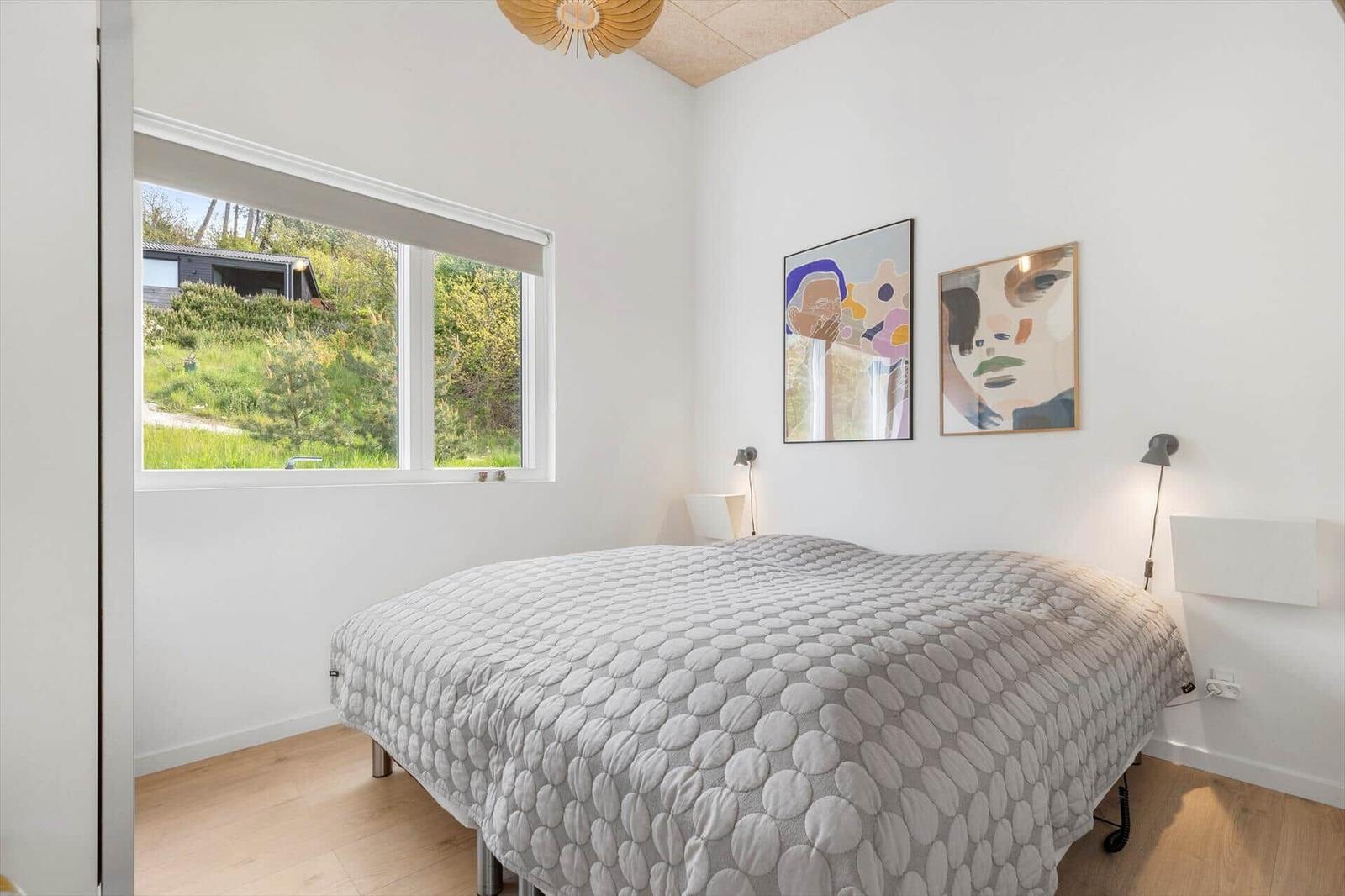 Schlafzimmer mit Bett, Fenster und Wandbildern.