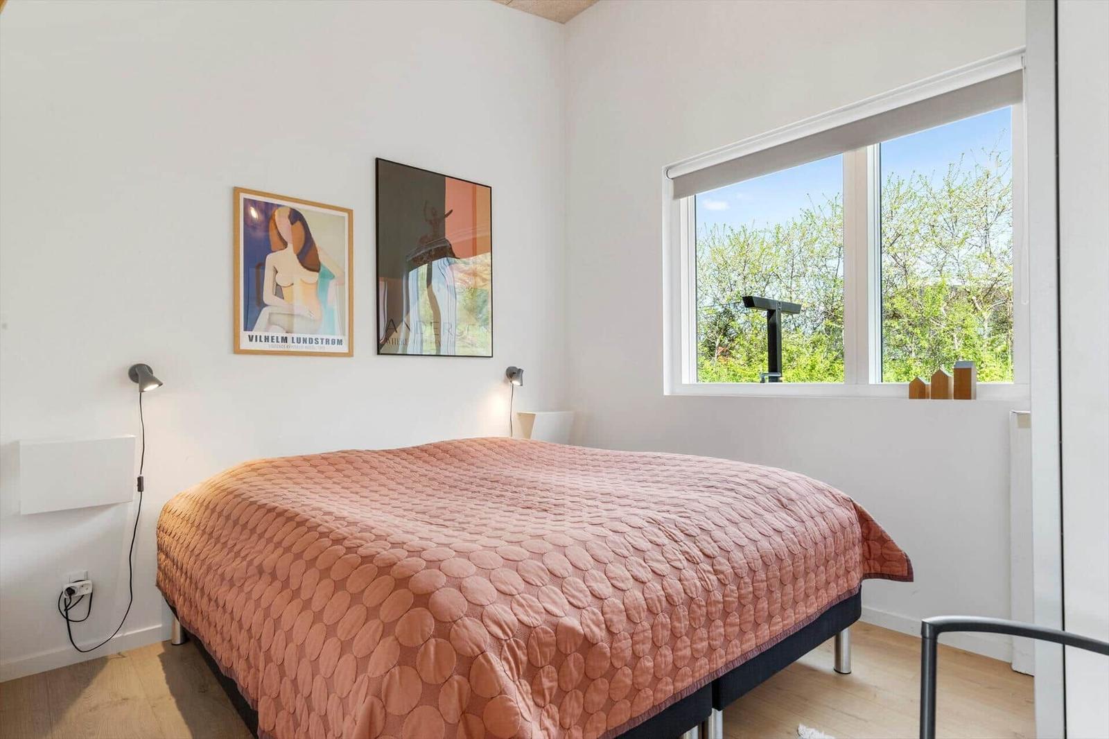 Schlafzimmer mit Bett, Fenster und Wandbildern.