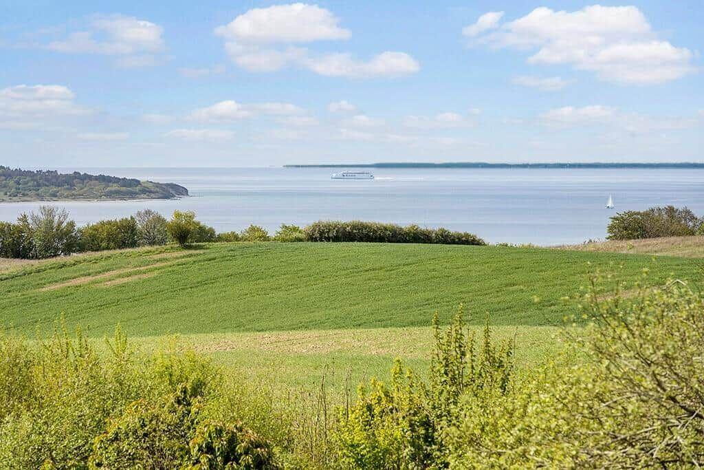 Weitläufiges Feld mit Blick auf ruhiges Wasser und Schiffe im Hintergrund.