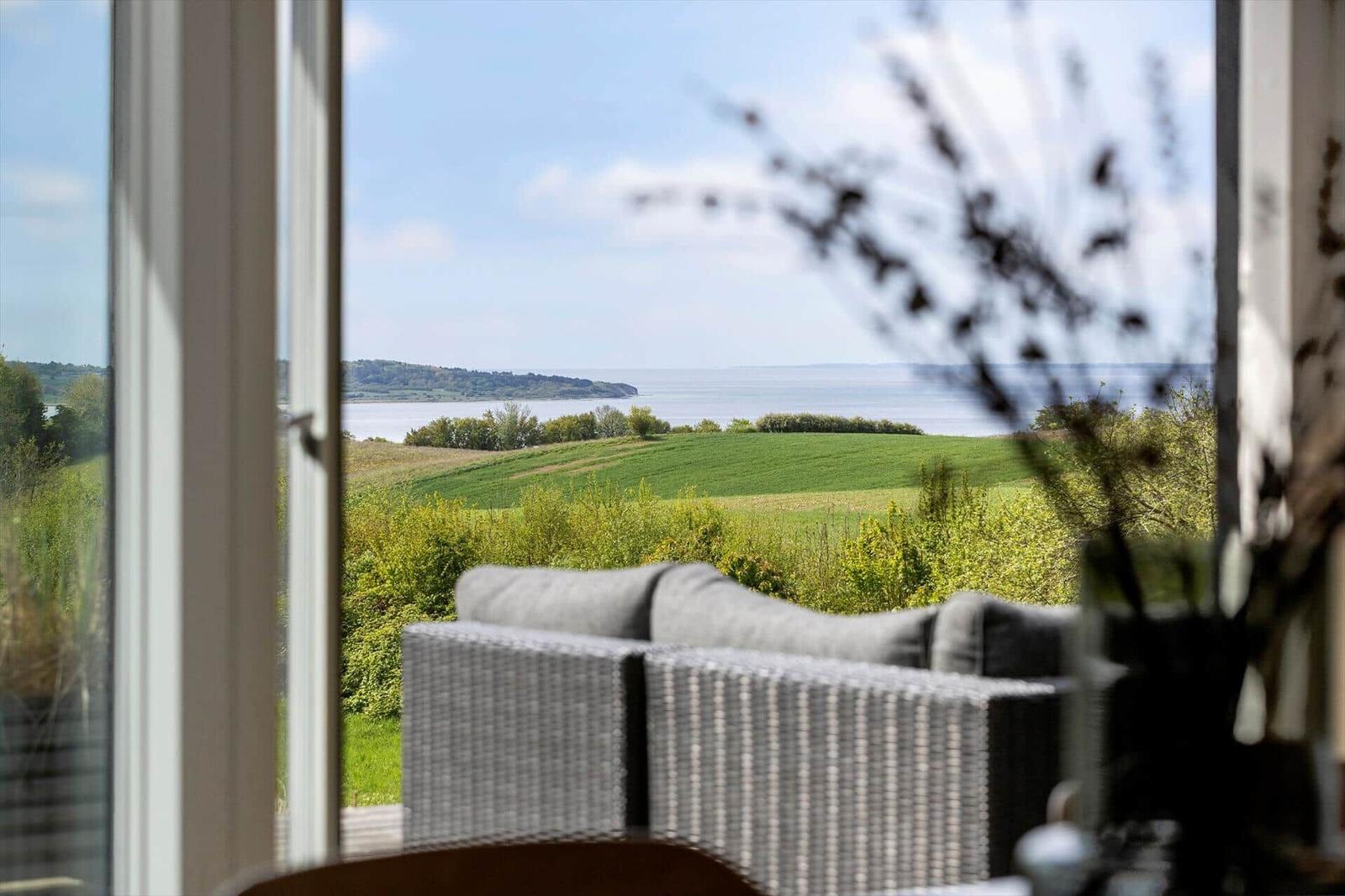 Von innen blickt man durch ein Fenster auf eine grüne Landschaft und einen See.