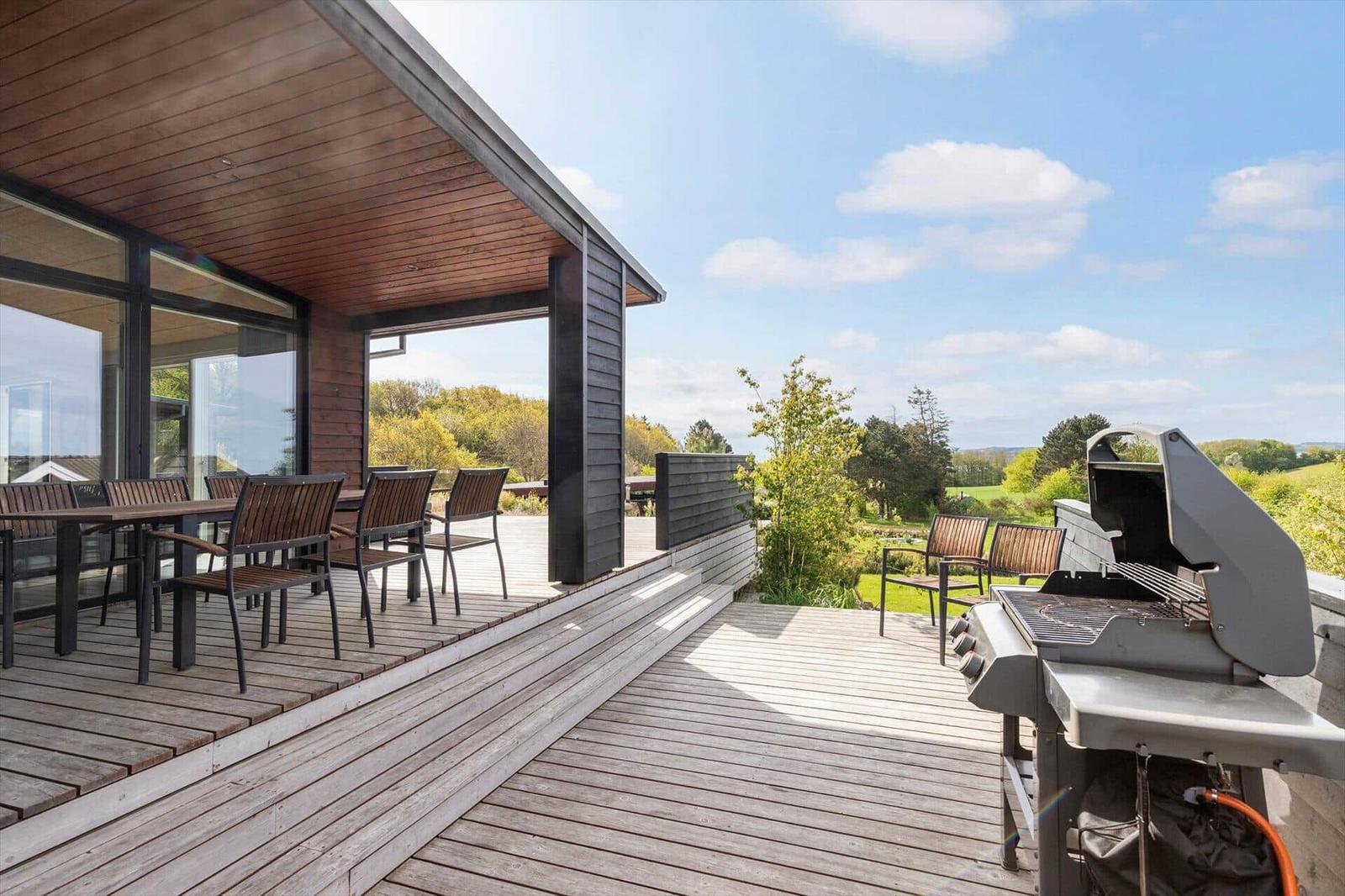 Terrasse mit Grill, Tisch und Stühlen. Blick auf grüne Landschaft.