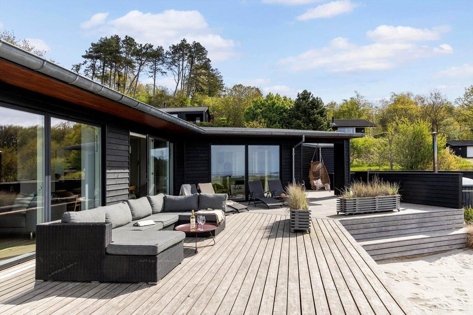 Großer Holzterrasse mit Lounge-Sofa, Liegen und Blick auf Wald.