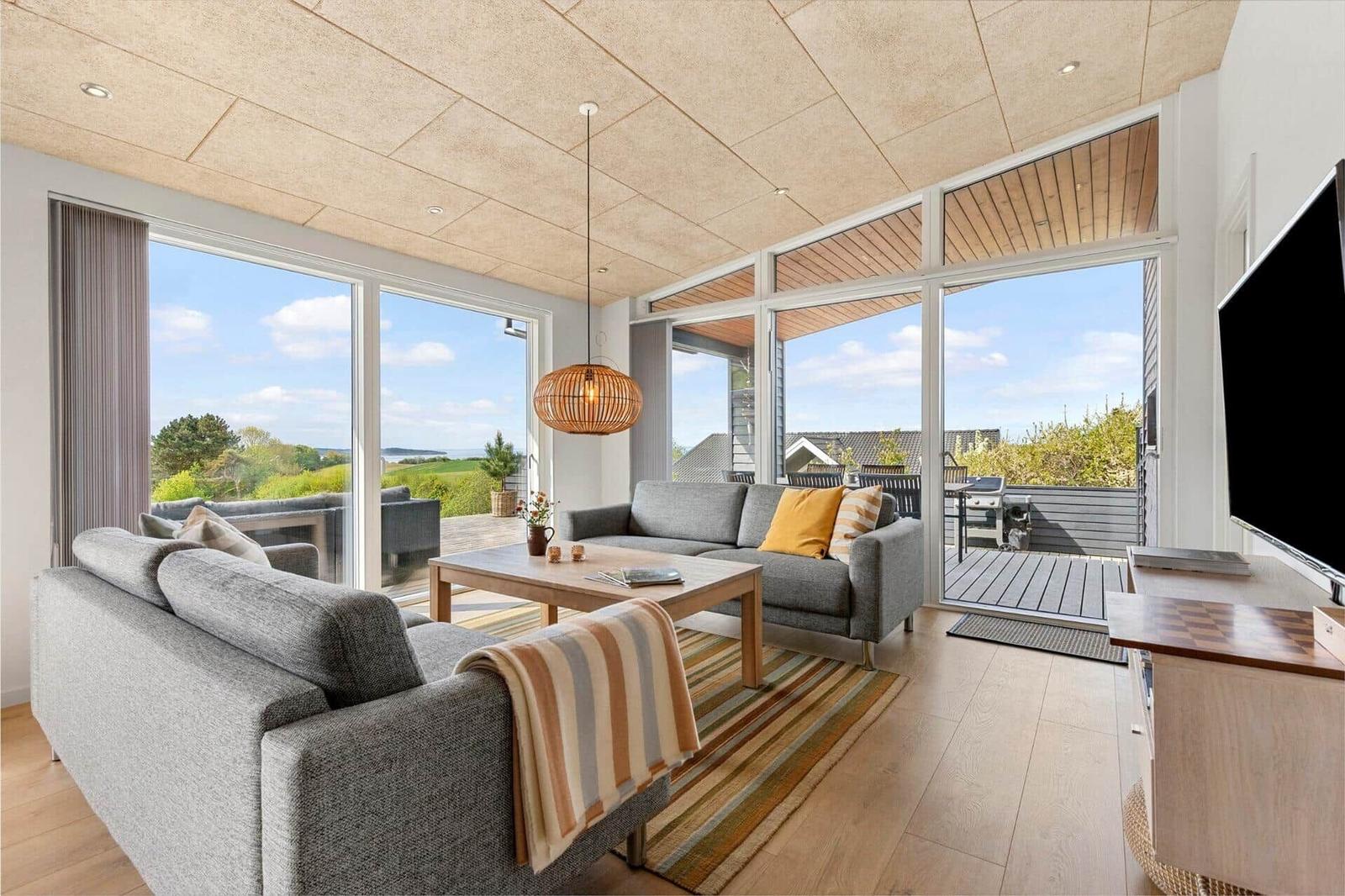 Wohnzimmer mit grauem Sofa, Holztisch und Blick auf Terrasse und Landschaft.