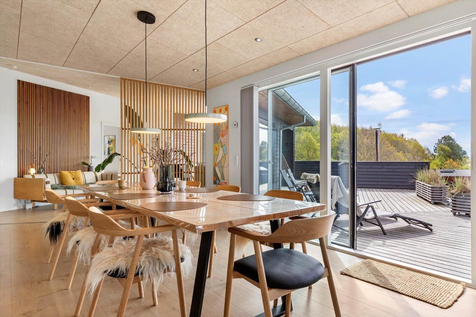 Essbereich mit Holztisch und Stühlen, große Glasfront zur Terrasse mit Blick auf Wald.