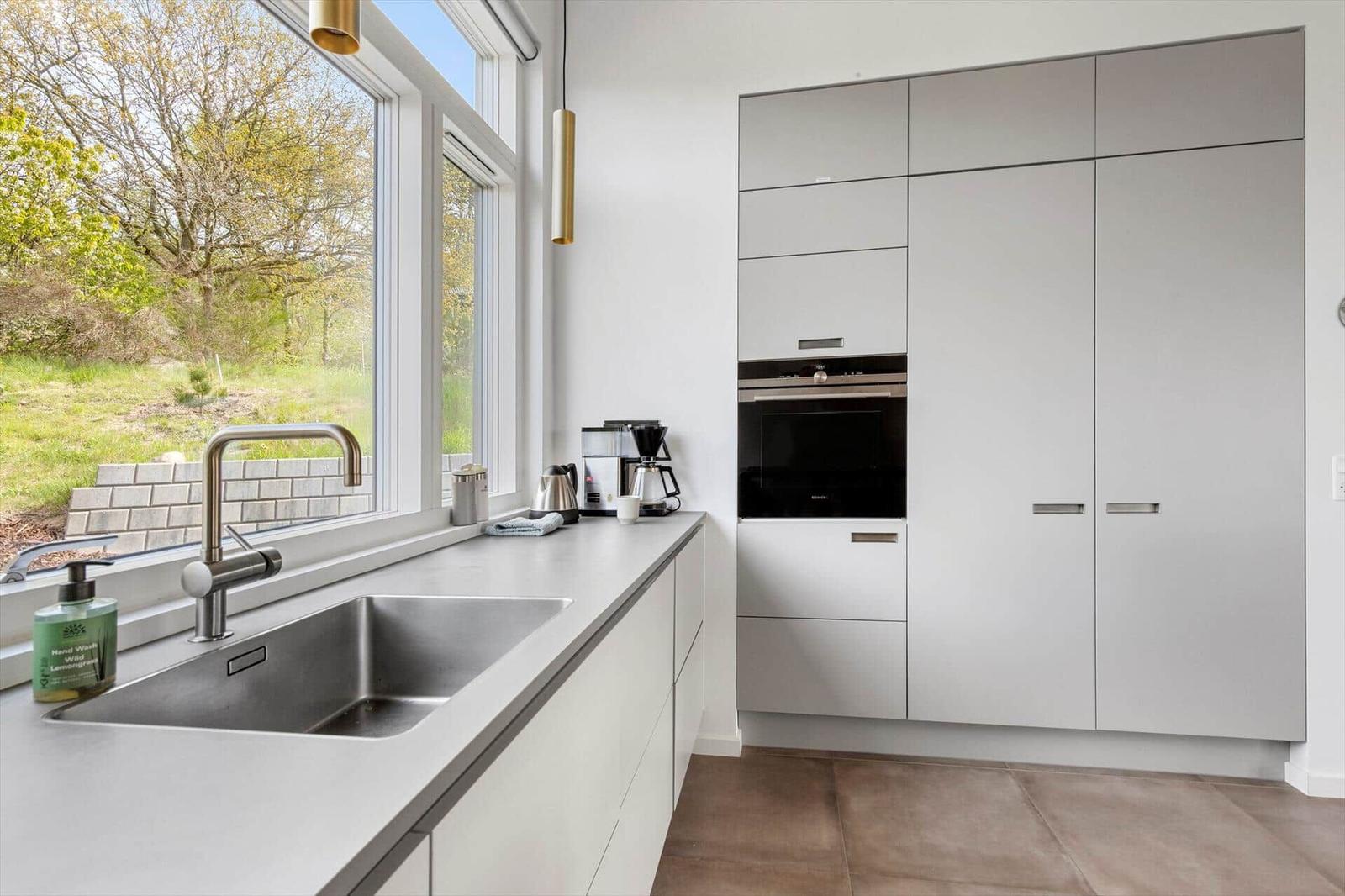Küche mit Fenster, Spüle und integriertem Ofen. Moderne Einbauküche mit grauen Schränken.