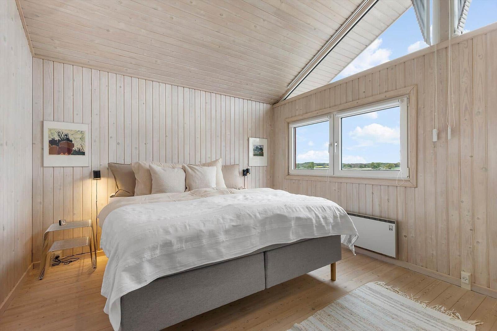 Schlafzimmer mit Bett, Fenstern und Holzwänden.