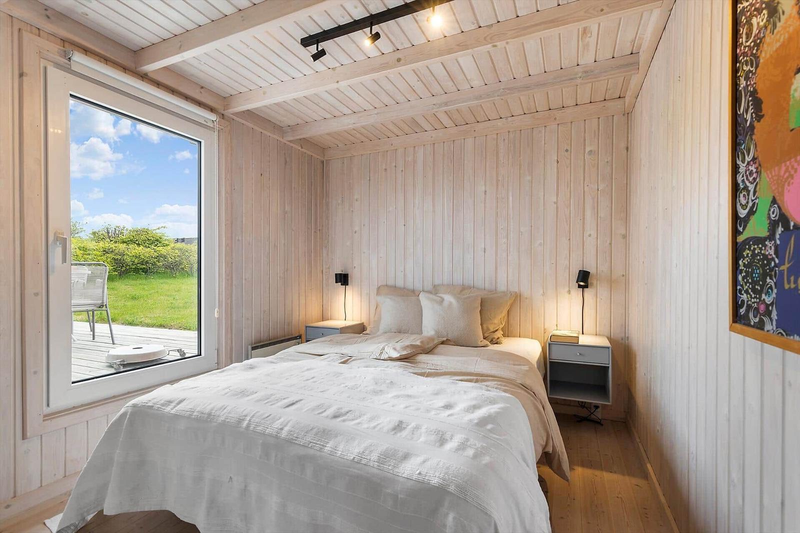Schlafzimmer mit Holzwand, Bett, Fenster und Nachttisch.