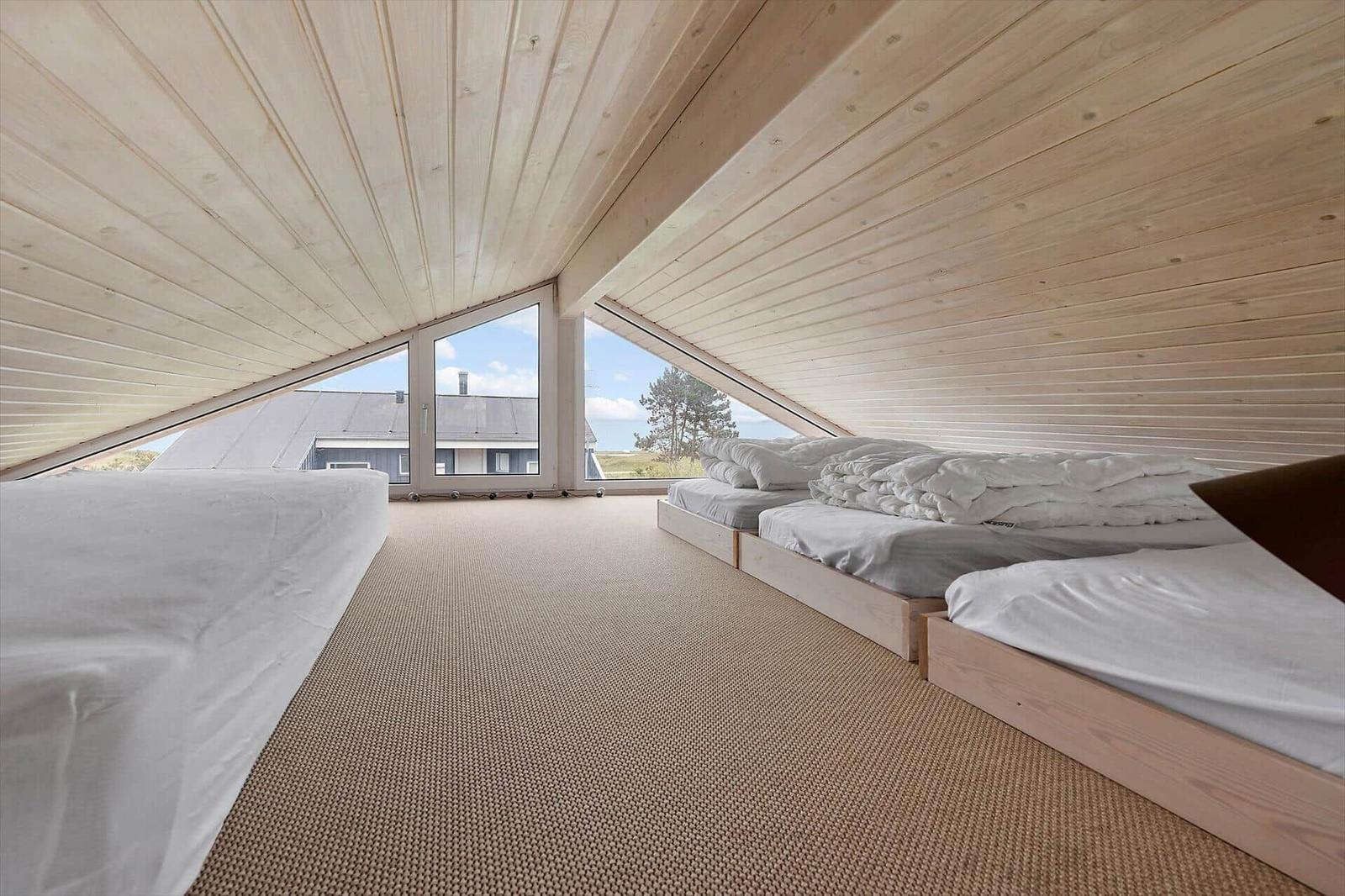 Schlafzimmer mit drei Betten unter Holzdecke und großem Fensterblick