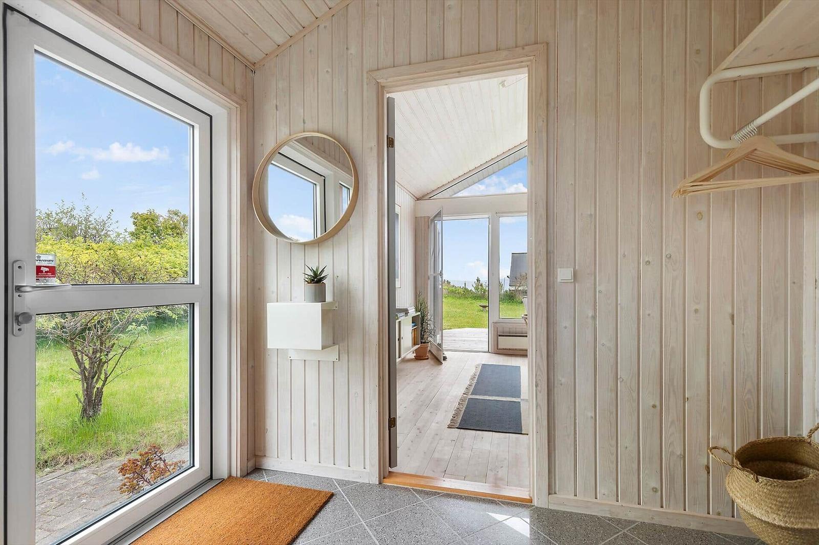 Eingangsbereich mit Holzwand, Tür zum Garten und runder Spiegel.