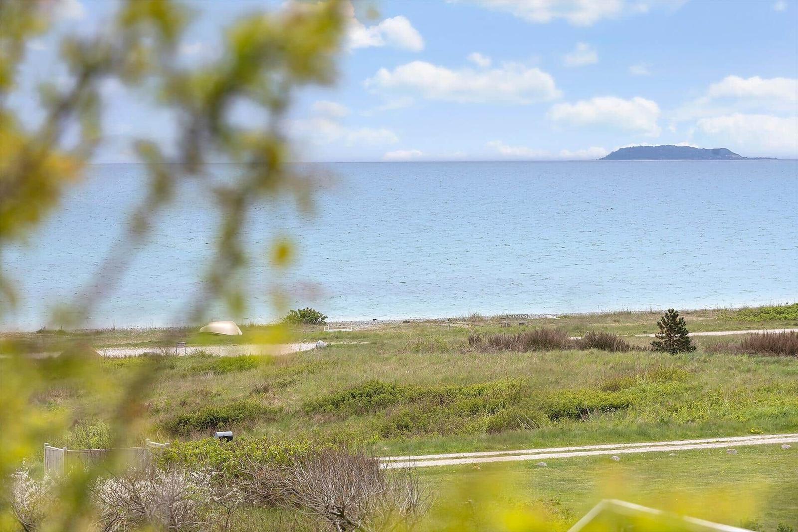 Meeresblick mit Insel im Hintergrund und grüner Landschaft im Vordergrund.