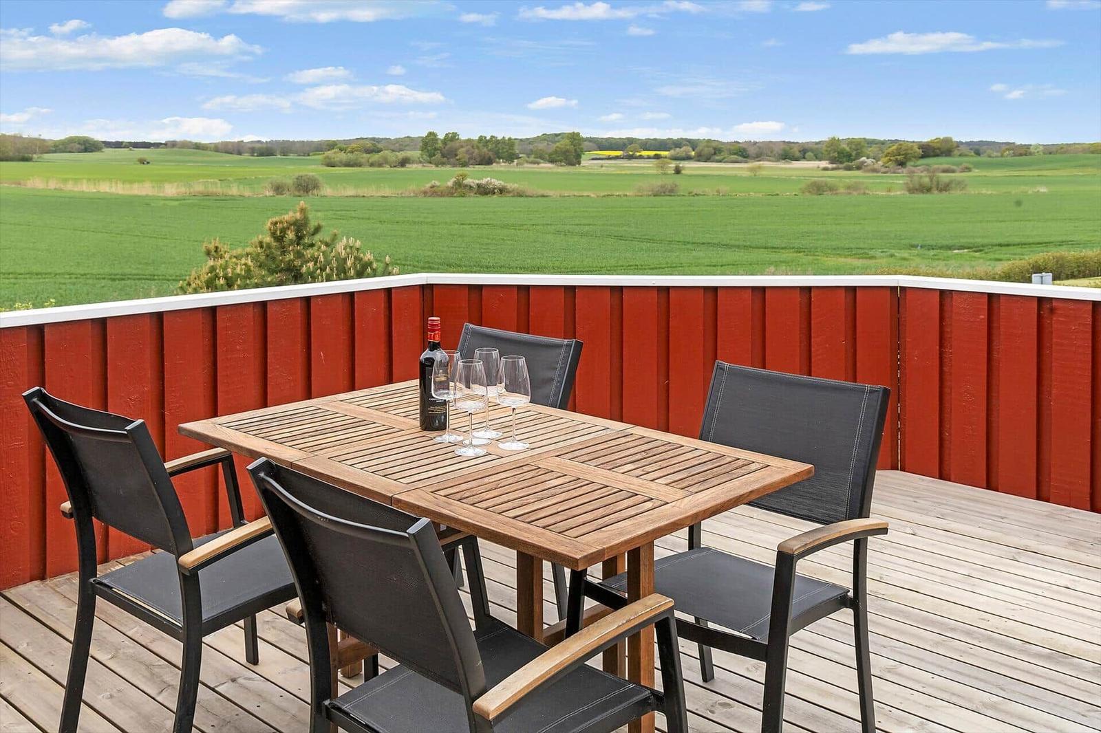 Terrasse mit Tisch und Stühlen, Blick auf grüne Felder.