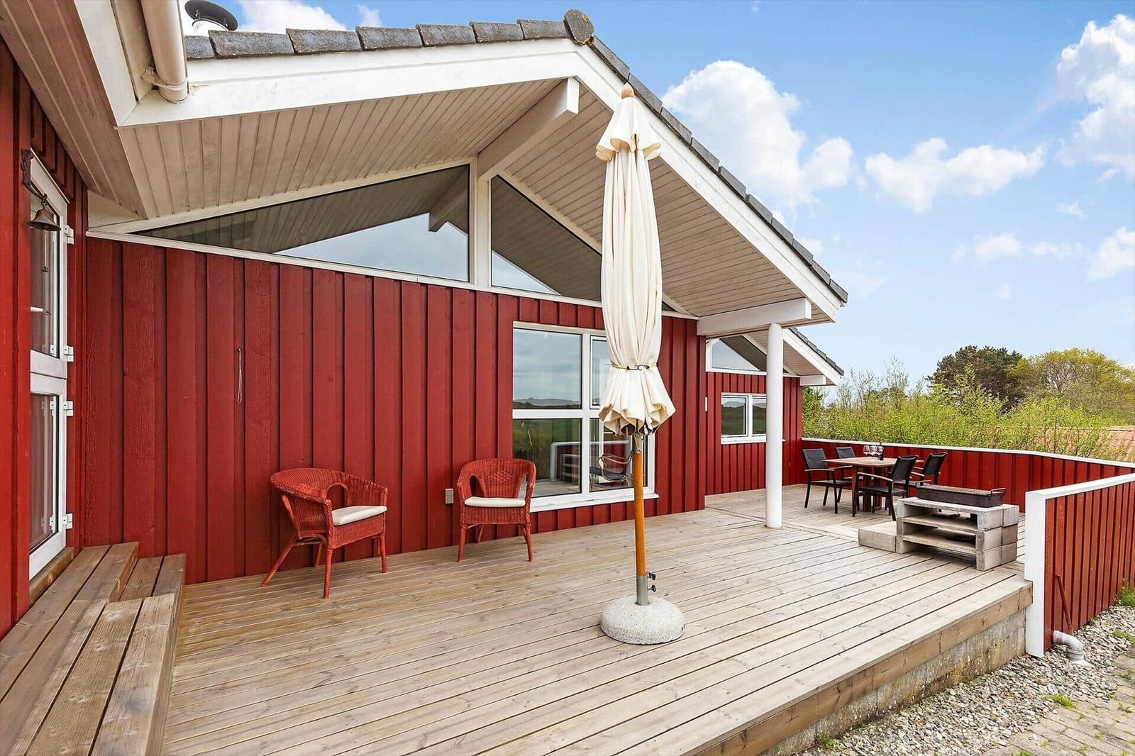 Roter Holzhaus mit Terrasse, Sonnenschirm und Sitzgelegenheiten.