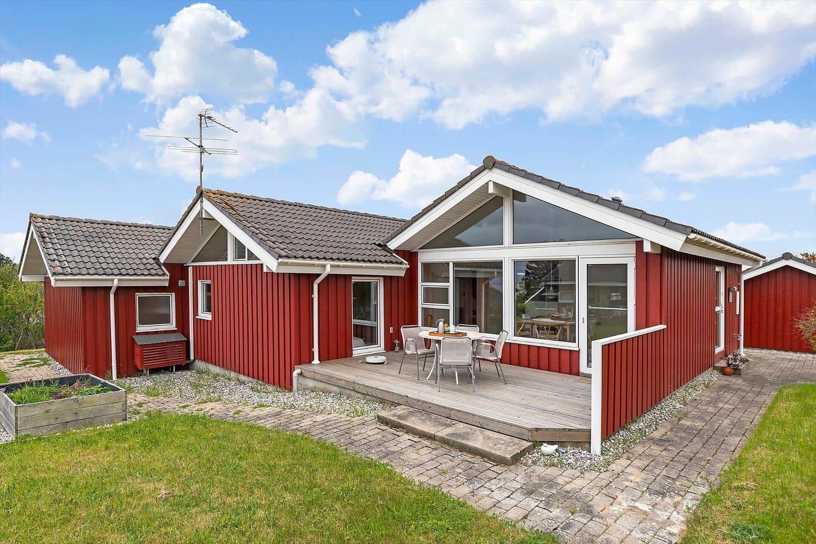 Rotes Ferienhaus mit Terrasse und Garten. Modernes Wohnzimmer mit großem Fenster.