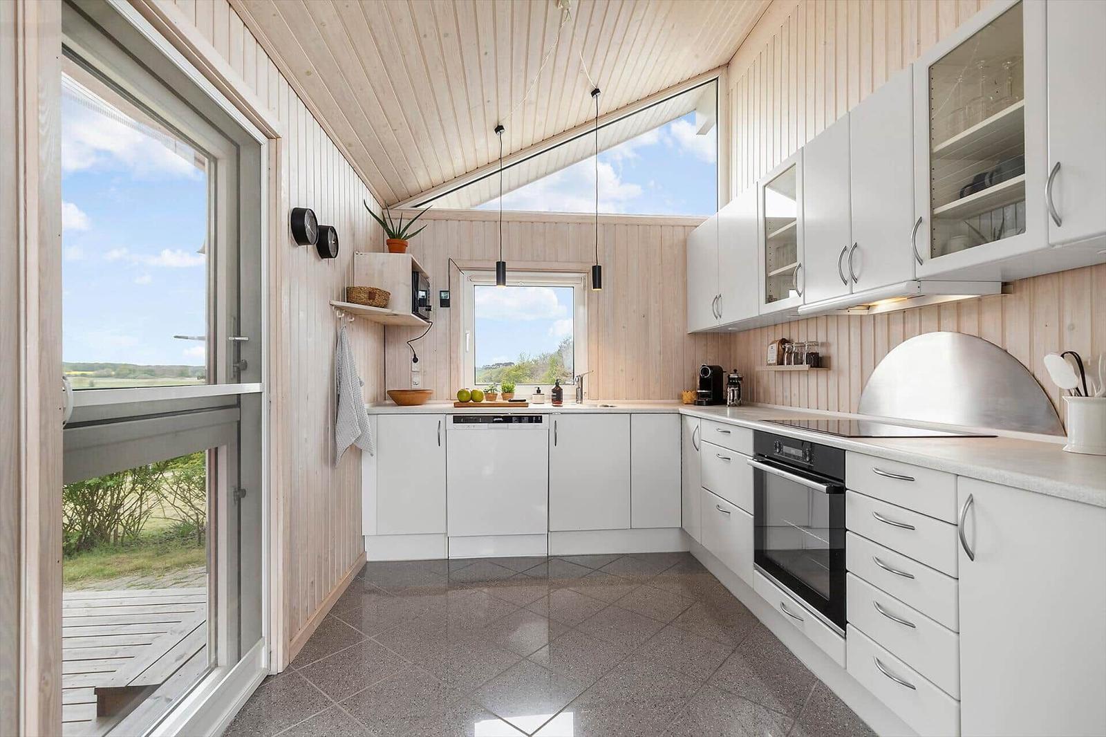 Moderne Küche mit weißen Schränken und Holzwänden. Große Fenster und Tür zur Terrasse.