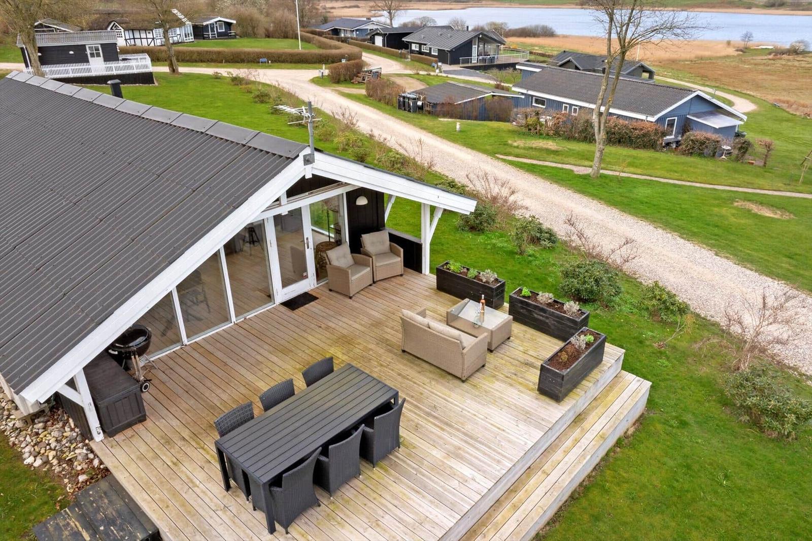 Deck with seating, dining table, and grill. View of green lawn and water.