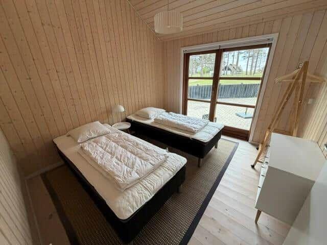 Two beds in a room with wooden walls and a window to the outdoor area.