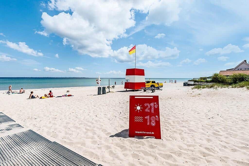 Beach with lifeguard station, weather sign, and bathers. Sand, sea, and clear sky.