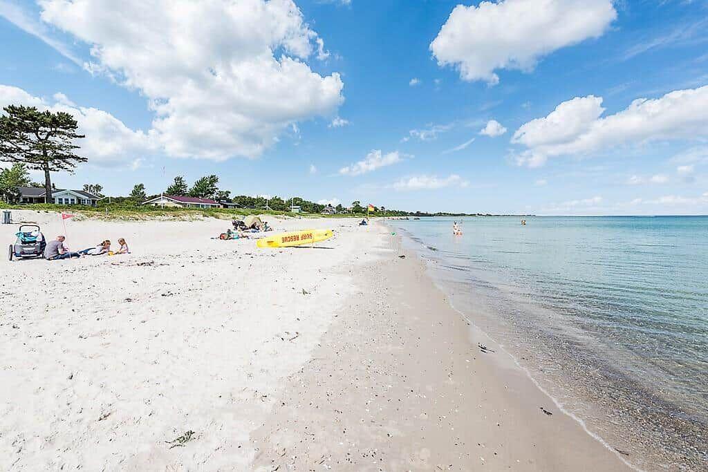 Beach with white sand and clear water, people relaxing and a rescue boat on the shore.