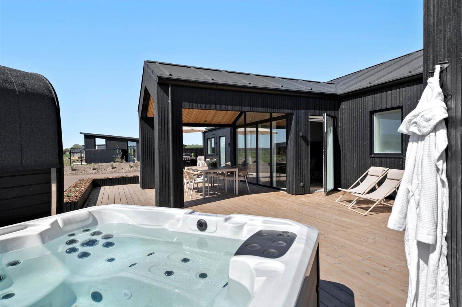 Outdoor area with hot tub, terrace, and lounge chairs in front of a modern house.