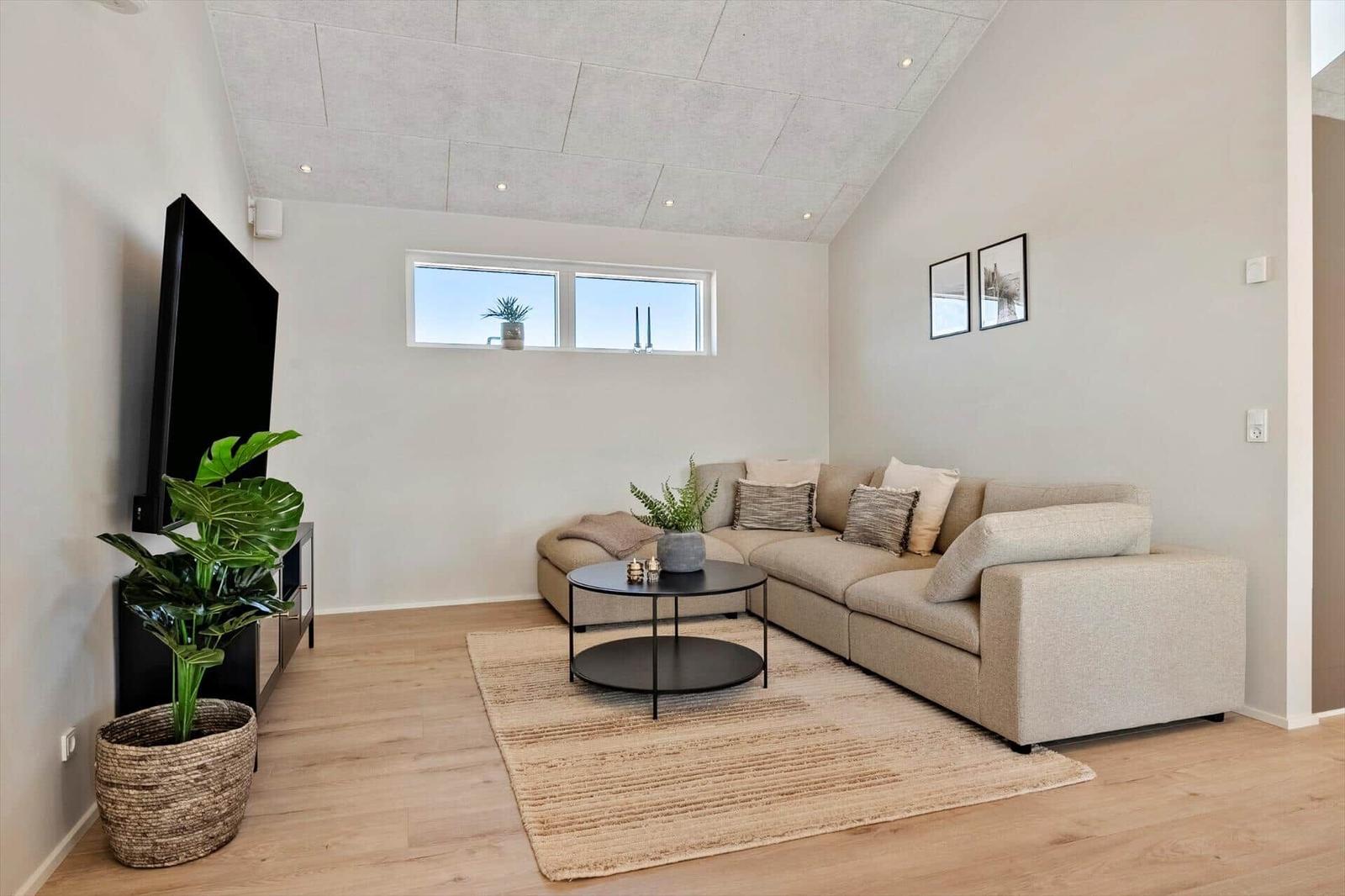 Living room with sofa, coffee table, and TV. Wooden floor and window with view.