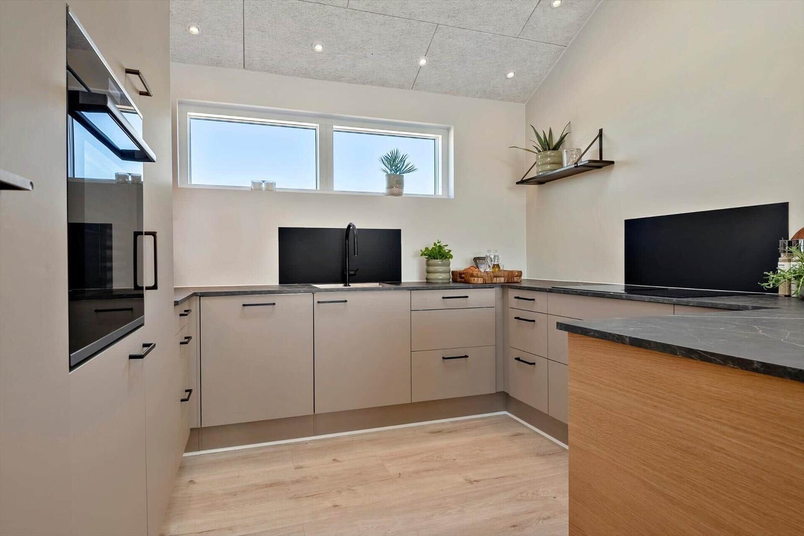 Modern kitchen with light cabinets, dark worktop, and window with plants.