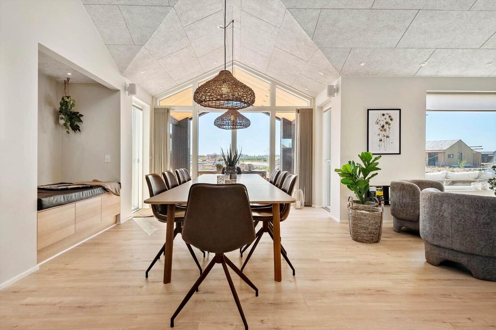 Dining area with long table and chairs, seating nook and living area with armchairs and plants.