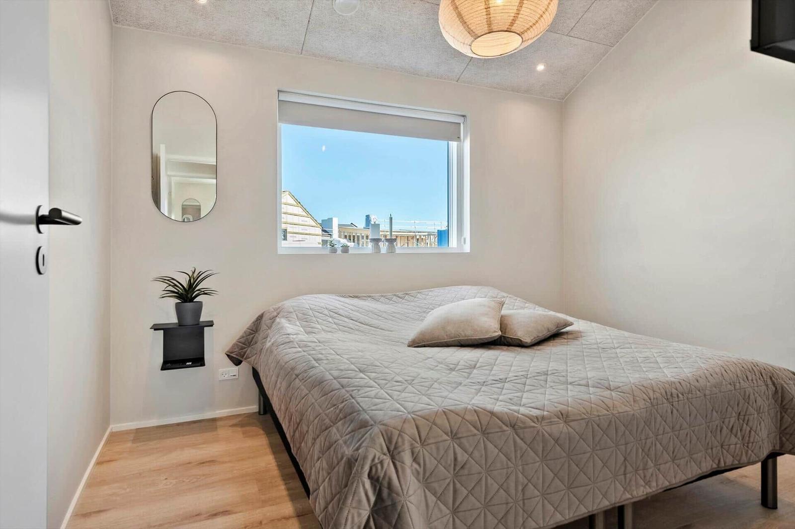 Bedroom with bed, window, and mirror on the wall.