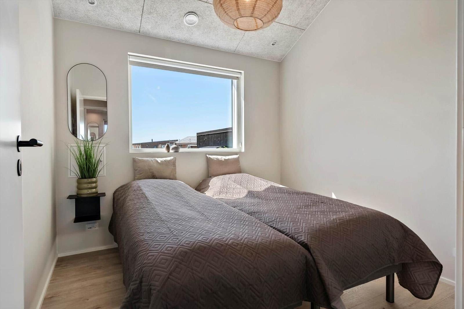 A bedroom with a double bed, window, and wall mirror. Wooden floor and ceiling light.