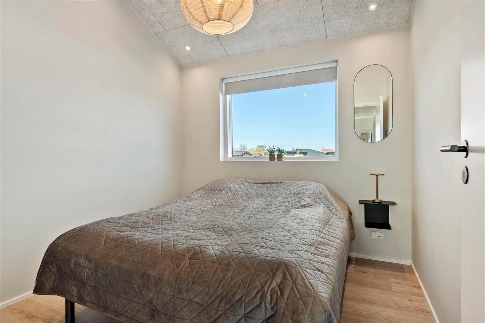 Bedroom with bed, window, and mirror on the wall.
