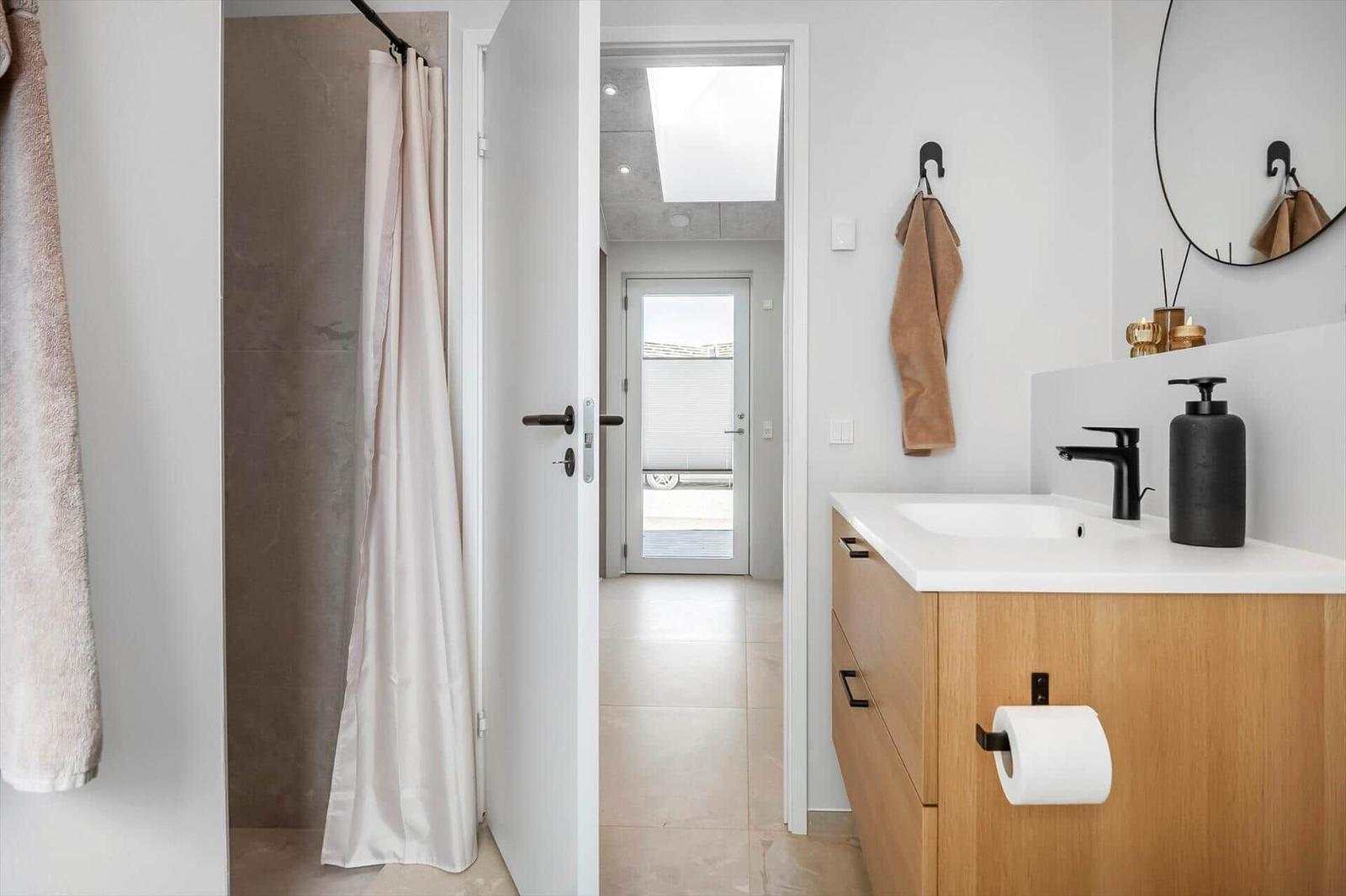 Bathroom with sink, shower, and mirror. Wooden cabinet and black fixtures.