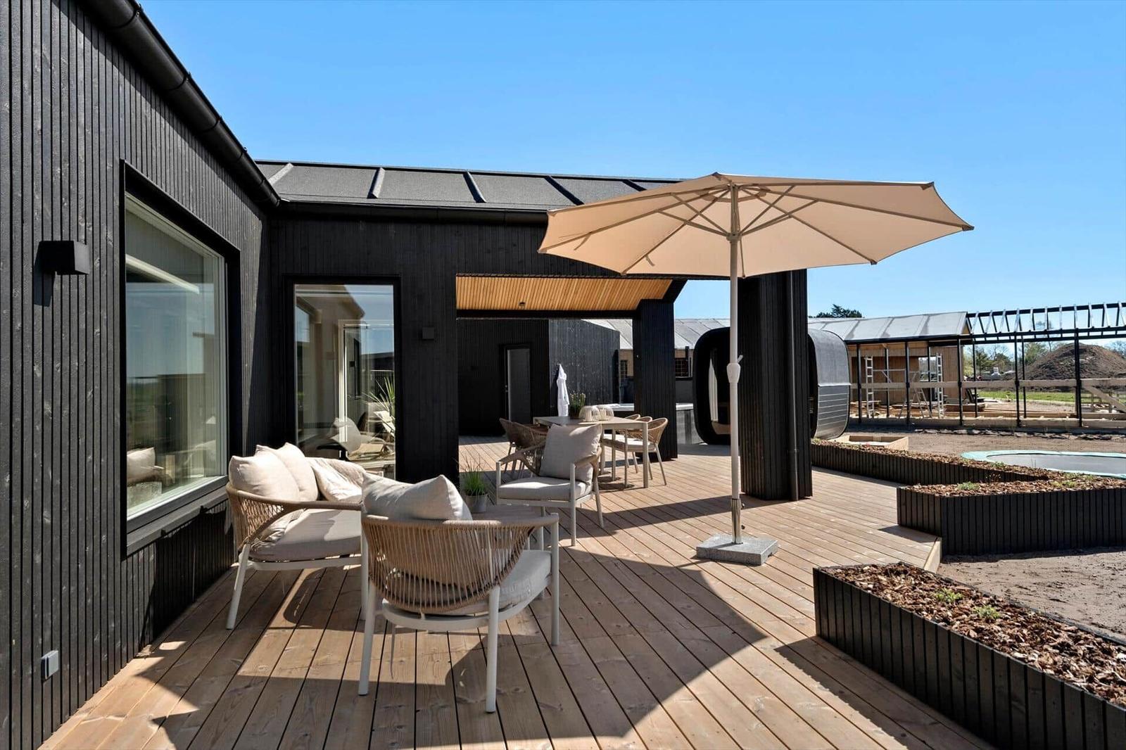 Terrace with seating, umbrella, and wooden deck. Modern house with large windows.