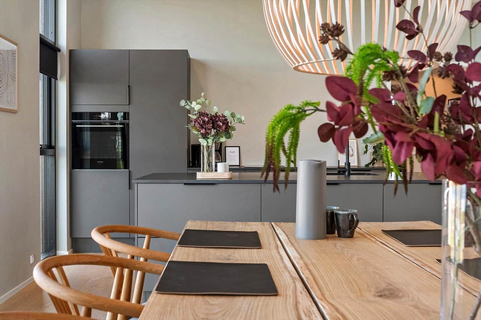 Dining area with wooden table, chairs, and modern kitchen in background.
