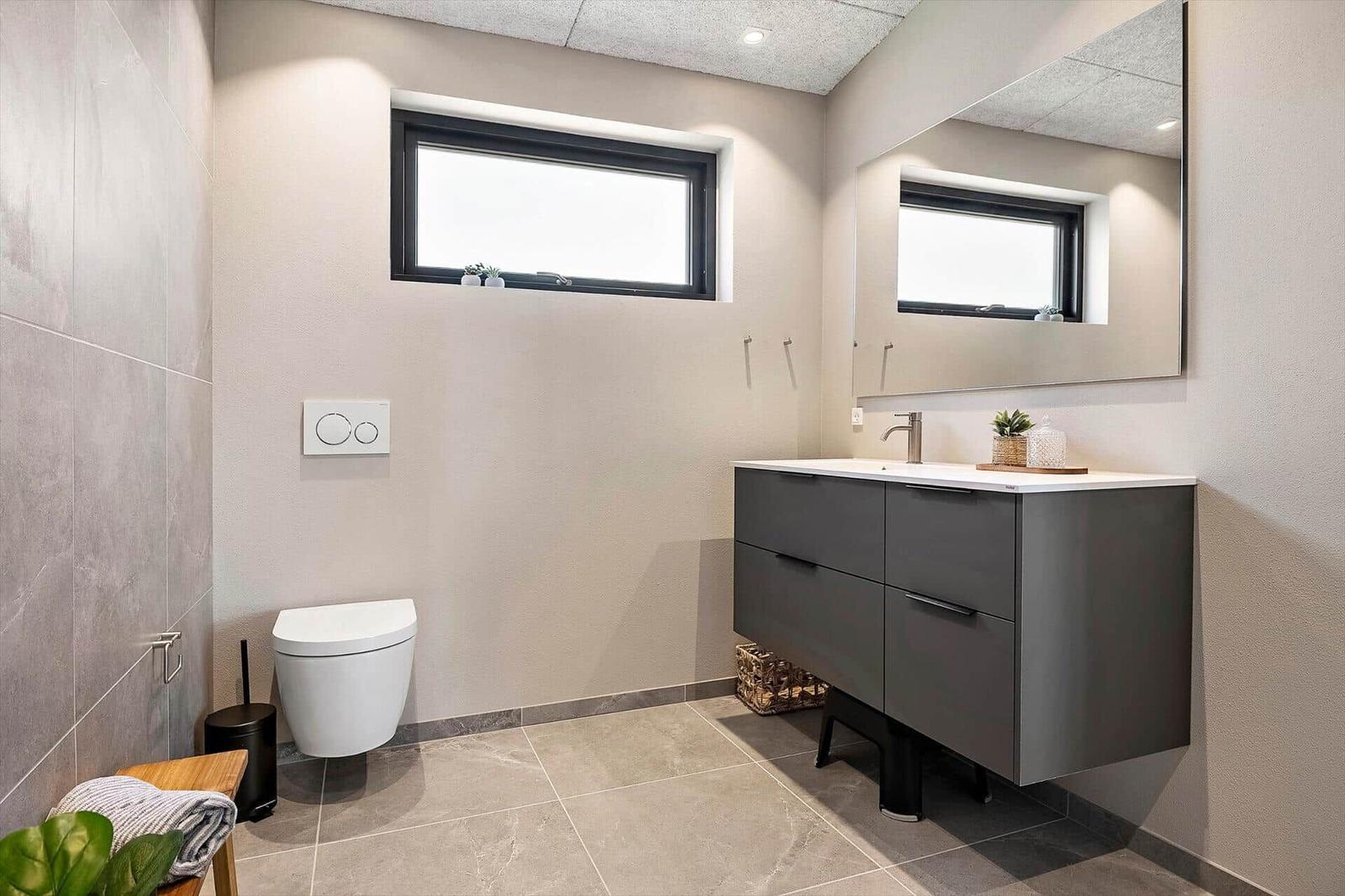 Bathroom with sink, mirror, toilet, and window.