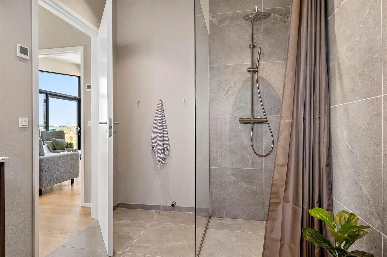Shower with glass enclosure and rain showerhead. View into living room with sofa.