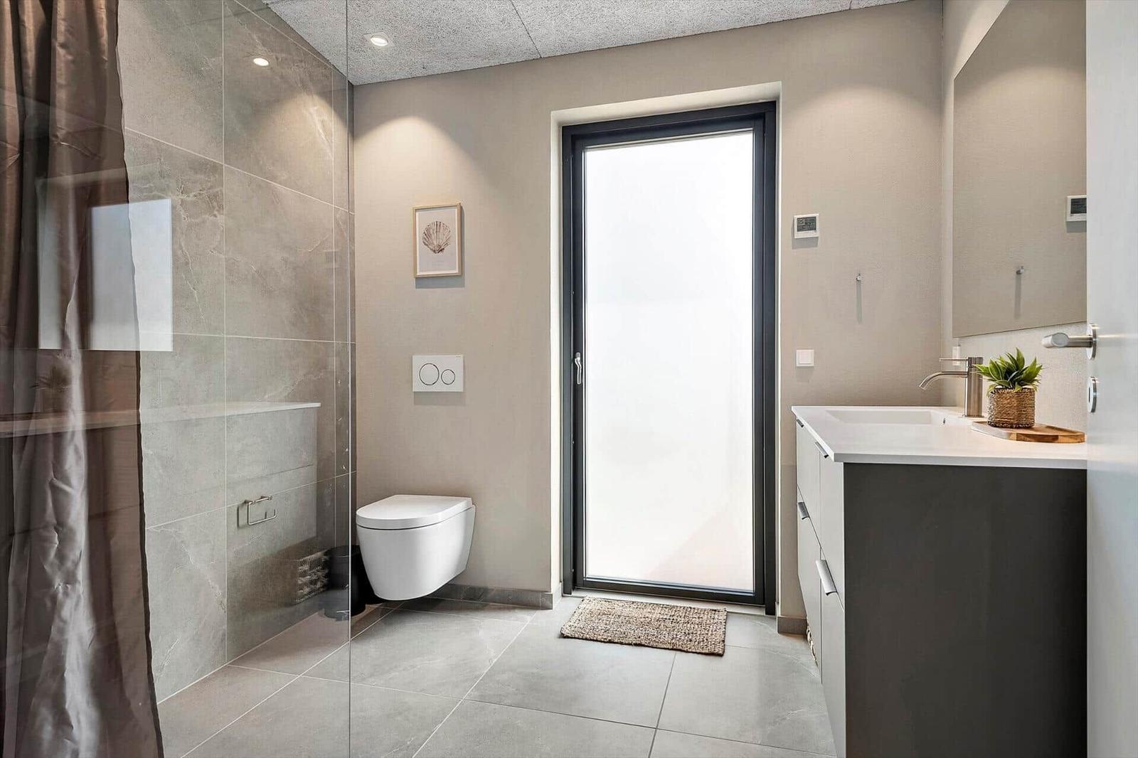 Bathroom with shower, toilet, and sink. Large window and modern design.