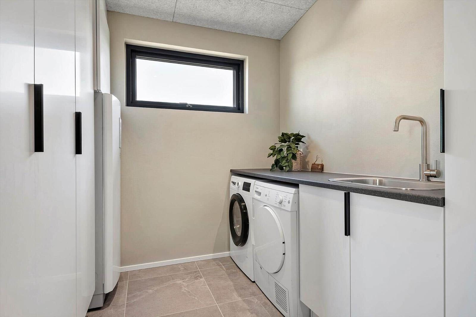 Laundry room with washing machine, dryer, and sink. Window and white cabinets.