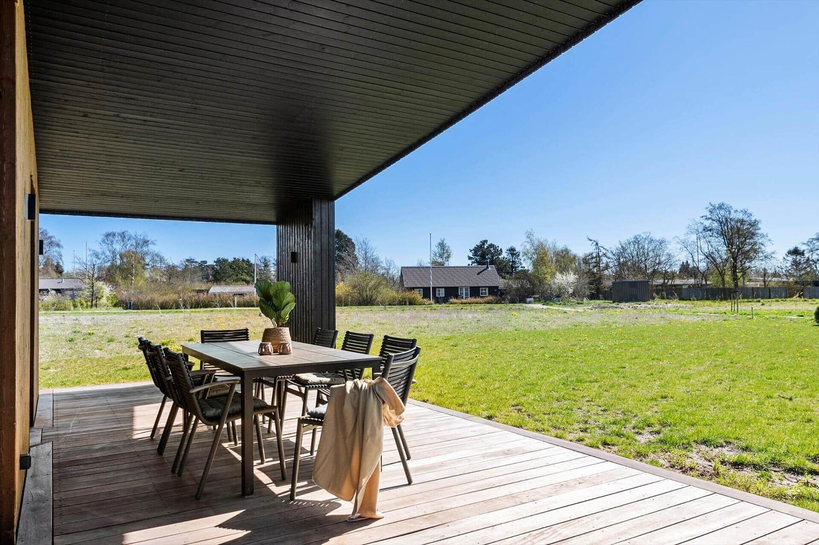 Patio with table and chairs, view of green field and sky.