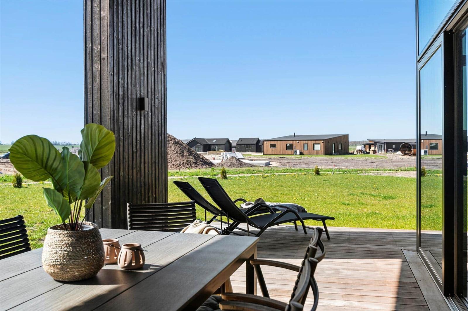 Deck with table, chairs, and lounge chairs. View of grassy area and modern houses in the background.